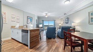 Une cuisine moderne avec un îlot central en bois, un coin repas comprenant une table et des chaises, et une vue sur l’extérieur grâce à une grande fenêtre.