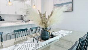 A modern kitchen with white cabinets, a dining table with chairs, and a vase with pampas grass on the table.