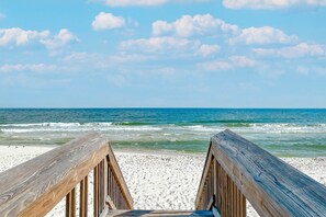 A wooden boardwalk leading to a sandy beach with ocean waves.