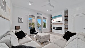 A modern living room with a sofa, ottoman, and a television mounted on the wall.