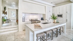 Une cuisine moderne avec des meubles blancs, un grand îlot central doté de tabourets, une cuisinière à gaz et un four à micro-ondes.