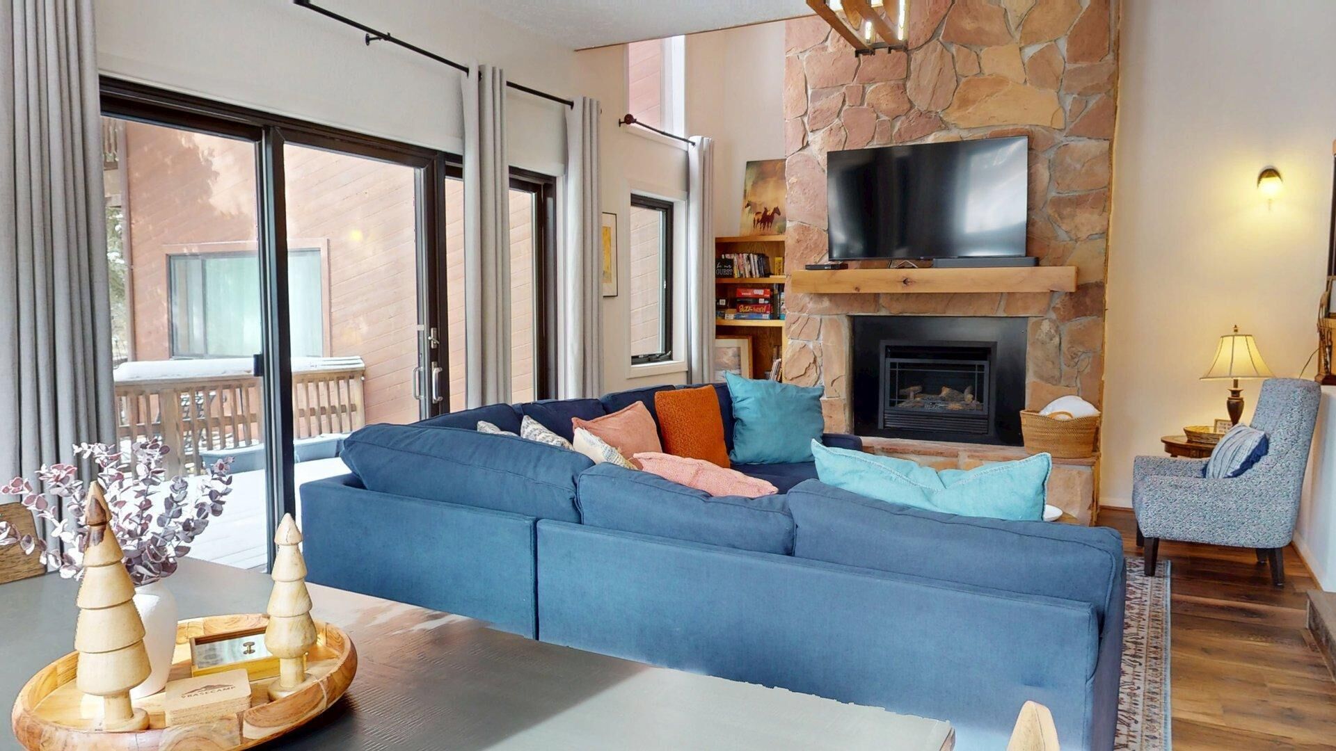 A modern living room with a stone fireplace, a large sofa, a television, and a balcony with a wooden railing.