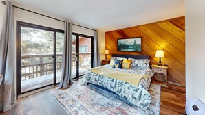 A bedroom with a large bed, a wooden ceiling, a painting on the wall, and a balcony with a view of trees. - Close to Lifts | Shuttle Stop | Renovated | Windswept 5 (Angel Fire)