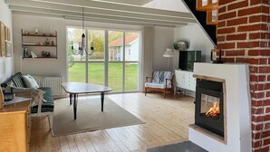 A cozy living room with a fireplace, wooden flooring, a dining table, and a sofa. - 4 bedroom cozy home in Beddingestrand (Beddingestrand)