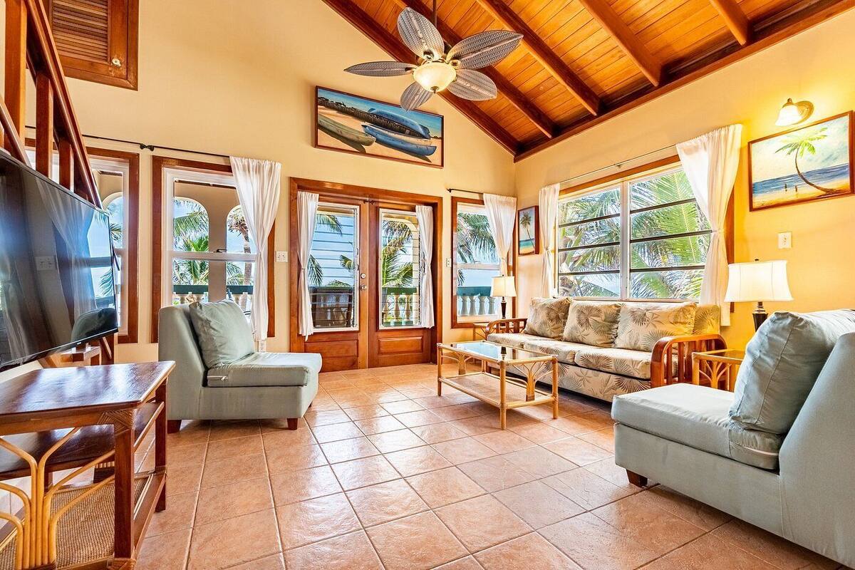 A spacious living room with a television, comfortable seating, and large windows offering views of palm trees.