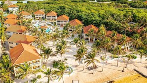Un complexe hôtelier comprenant plusieurs bâtiments, un espace piscine et une plage bordée de palmiers.