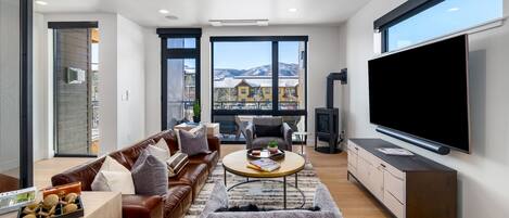 Una sala de estar moderna con un televisor grande, sofás de cuero, una mesa de centro y vistas a las montañas a través de amplios ventanales.
