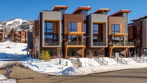 A modern multi-story building with balconies, large windows, and a snowy landscape in the background. - Urban Reserve, AC! Upscale, Private Rooftop Hot Tub & Deck Area with Views! (Steamboat Springs)