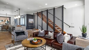 A modern living room with a leather sofa, a round coffee table, and a staircase with a mesh partition. - Urban Reserve, AC! Upscale, Private Rooftop Hot Tub & Deck Area with Views! (Steamboat Springs)