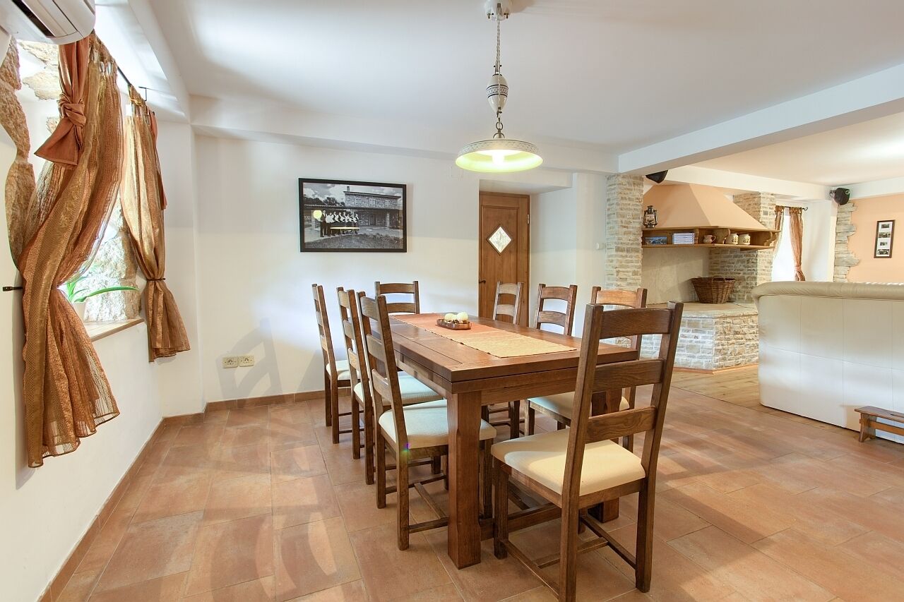 Un coin repas avec une table et des chaises en bois, un luminaire suspendu, un tableau encadré au mur et un mur en briques avec une étagère.
