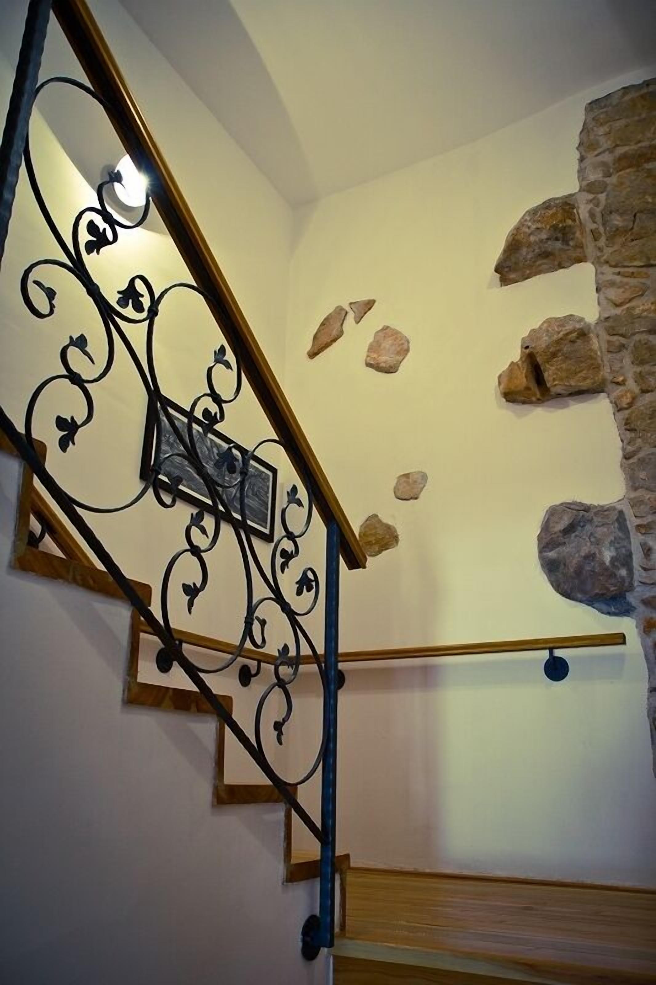 A staircase with a wrought iron railing, a stone wall, and a wooden floor.