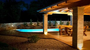 An outdoor pool area with stone walls, wooden pergola, and a dining table with chairs. - Villa Mediterana (Kvarner - Kras) (Kras)