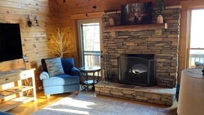 A cozy cabin interior with a stone fireplace, a blue sofa, a television, and a wooden ceiling. - Gratitude View - It's cooler in the mountains! (Ararat)