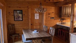 A wooden interior with a dining table, chairs, a chandelier, and a kitchen area. - Gratitude View - It's cooler in the mountains! (Ararat)