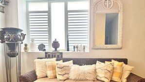 A cozy living room with a brown wicker sofa, a tall floor lamp, and a large window with blinds.