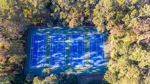 Vue aérienne d’un court de tennis entouré d’une forêt dense.