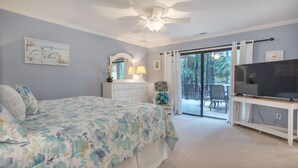 Un dormitorio con cama, cómoda, televisor y un balcón con mobiliario exterior.