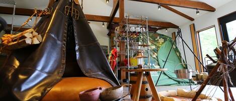 A rustic interior with a hammock, wooden stools, and a hanging rack with various items.