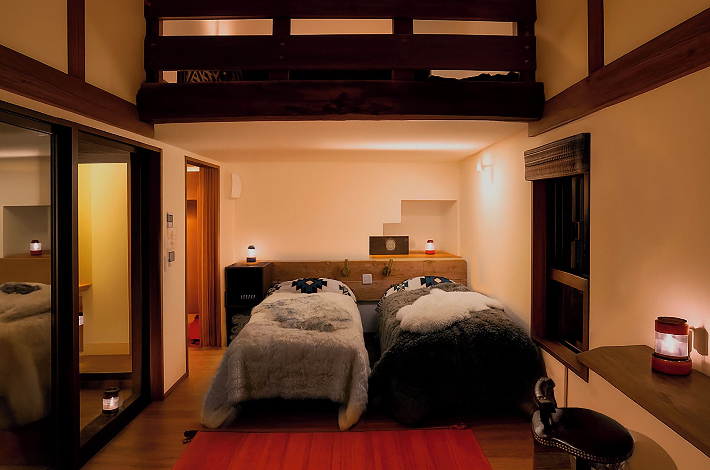 A cozy room with two beds, a small table, a mirror, and a window.