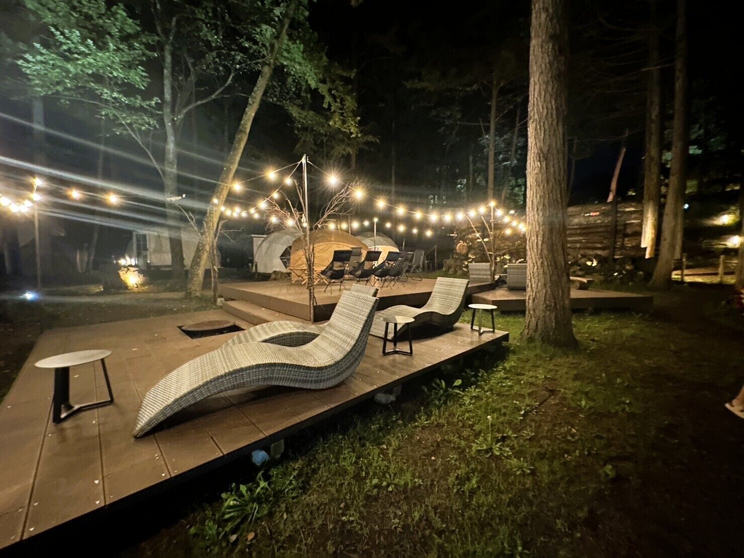 Area esterna con sedute lounge e tavoli, circondata da alberi e luci decorative.
