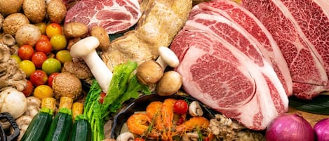 A variety of fresh produce and meats, including tomatoes, mushrooms, and different cuts of beef, arranged on a wooden surface.