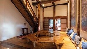A spacious room with a high ceiling, exposed wooden beams, a central wooden table, a sofa with cushions, and a view into another room with a window. - Hanz Outdoor Resort (formerly Glamping Villa Hanz Kawaguchiko) (Fujikawaguchiko)