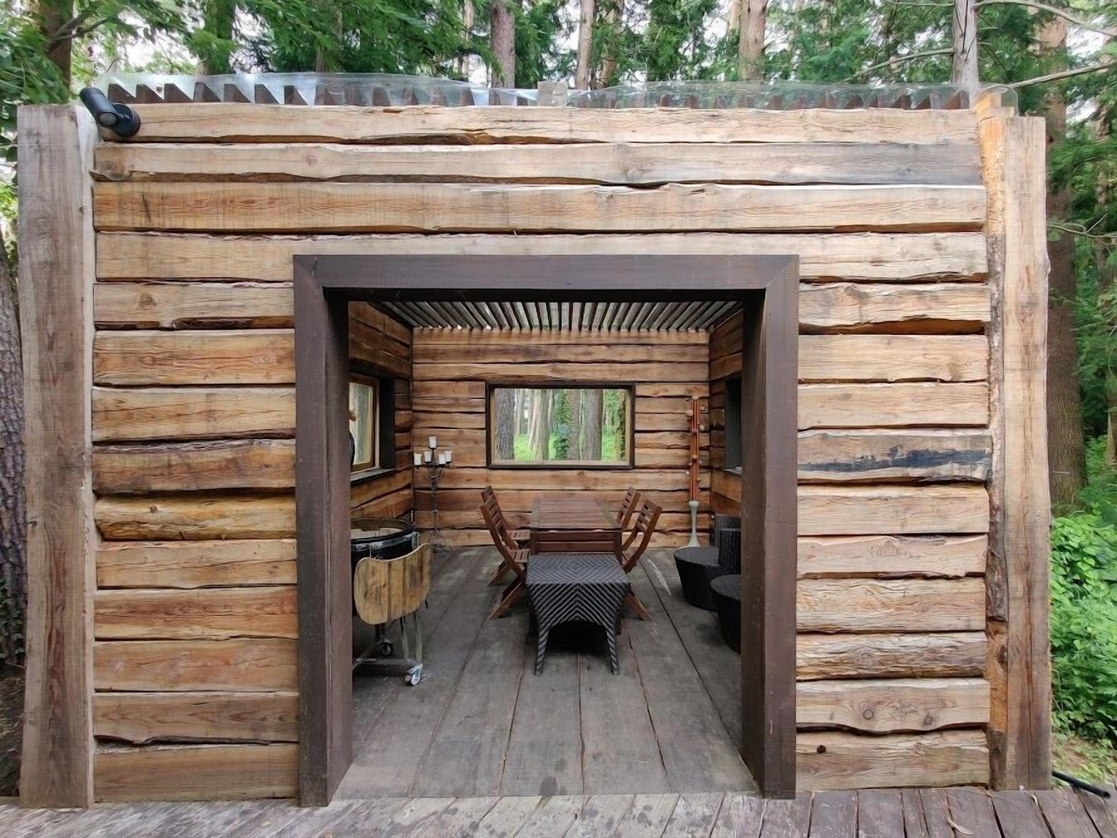 A log cabin with a central dining area featuring a table and chairs, surrounded by wooden walls and a window.