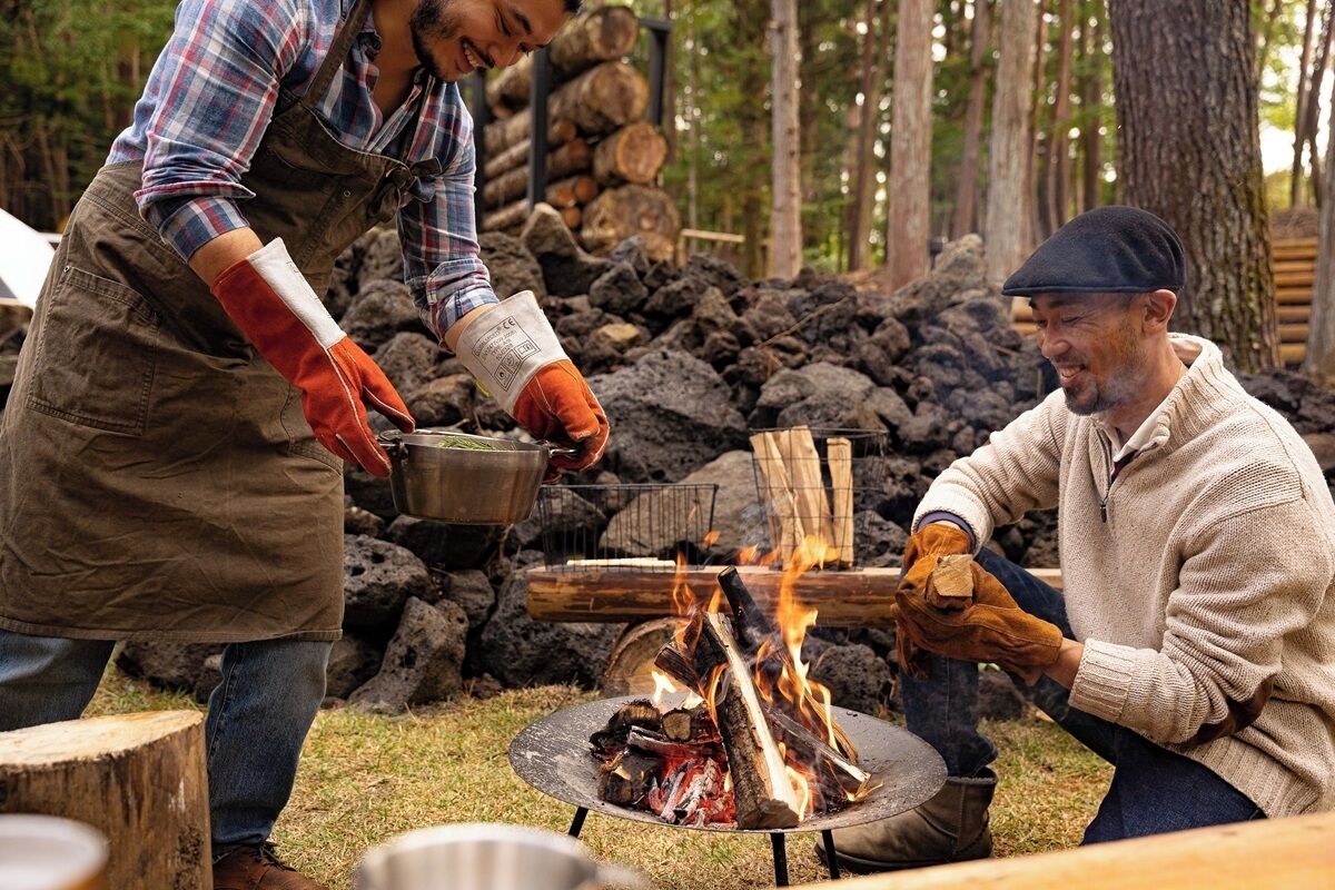 Two people around a campfire with logs and a pot.