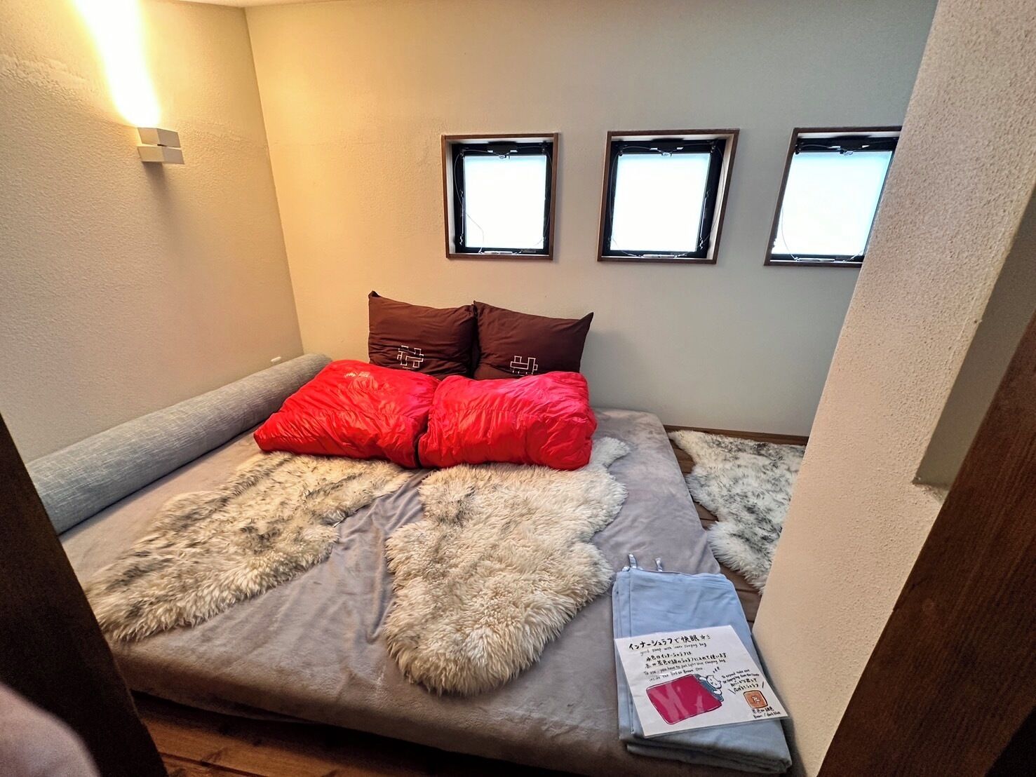 A small, cozy room with a bed, a fluffy rug, and three wall-mounted windows.