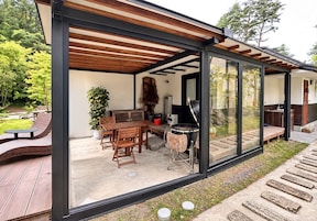 A modern outdoor dining area with a wooden table and chairs, a grill, and a potted plant.