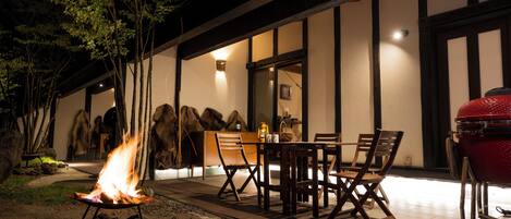 Un espacio al aire libre para comer con un brasero, sillas de madera y una parrilla.