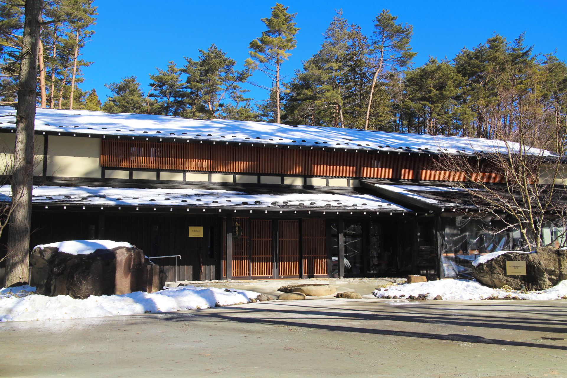 A traditional Japanese building with a snow-covered roof, wooden exterior, and a stone pathway leading to the entrance.