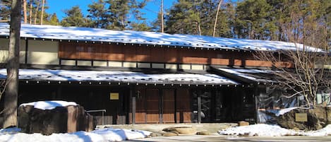 A traditional Japanese building with a snow-covered roof, wooden exterior, and a stone pathway leading to the entrance.
