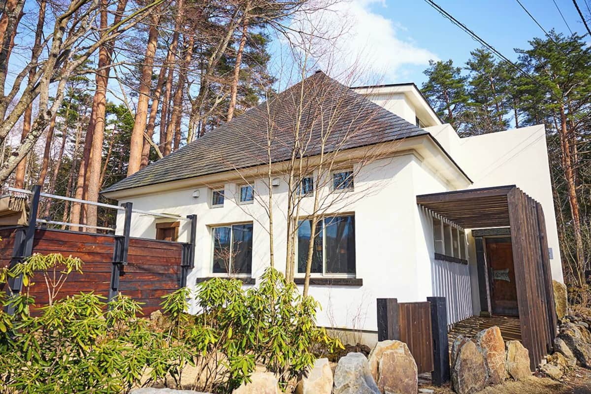 Une maison moderne à deux étages, avec une façade blanche, de grandes fenêtres et une terrasse en bois.