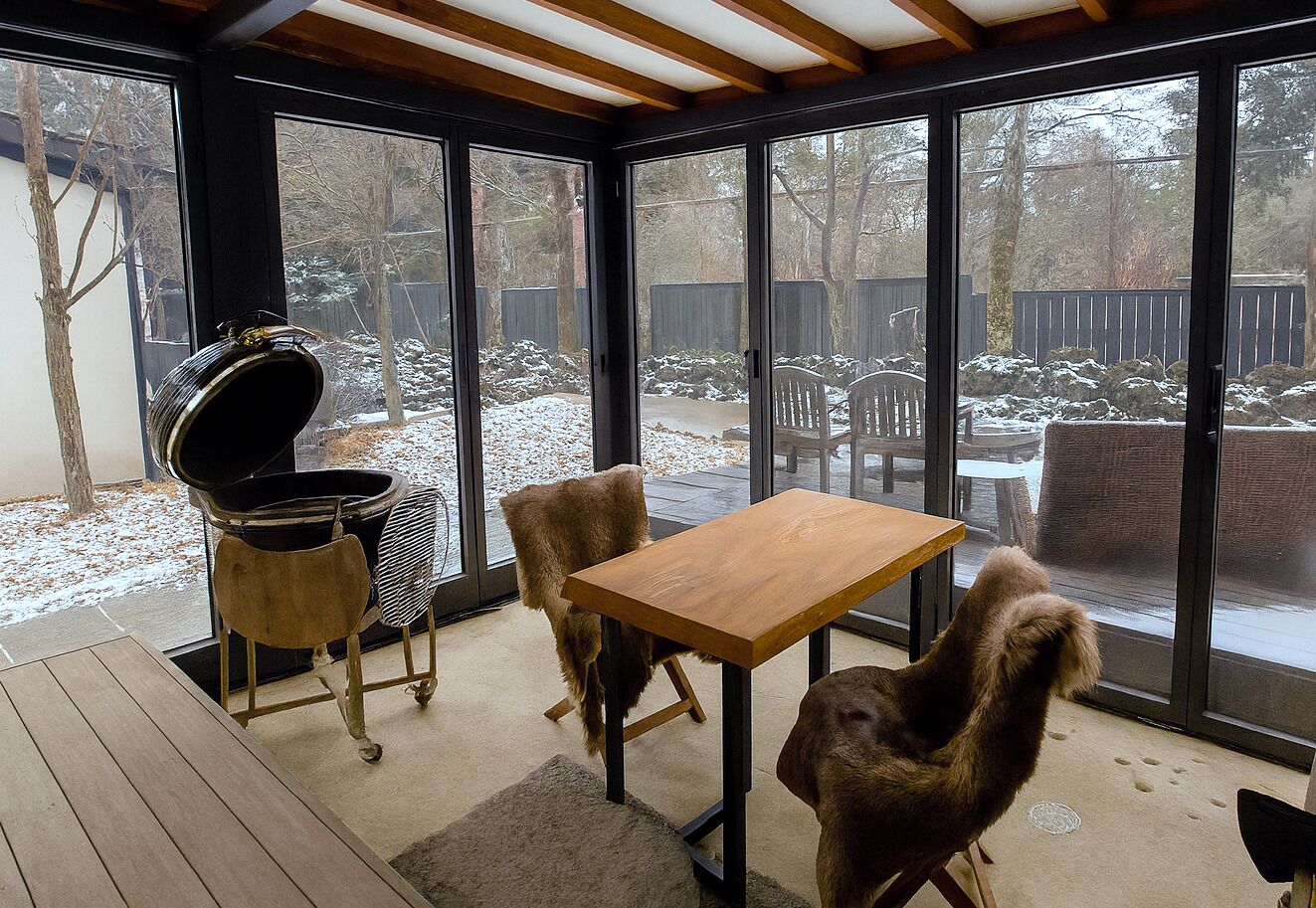 Ein überdachter Außenbereich mit Holztisch und -stühlen, einem Grill und Blick auf einen verschneiten Garten.