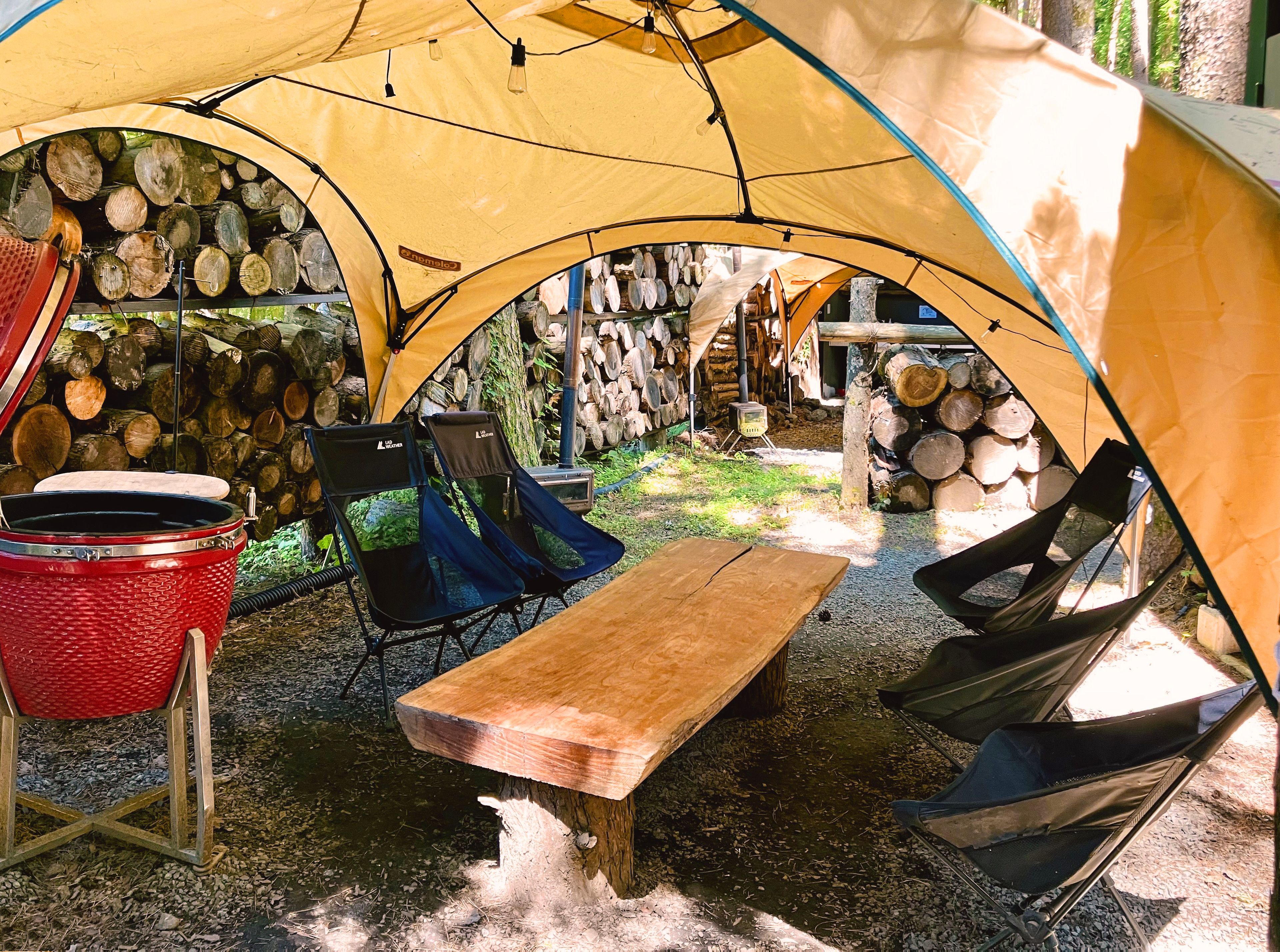 Ein Campingplatz mit Zelt, Picknicktisch, Stühlen und einer roten Kühlbox.