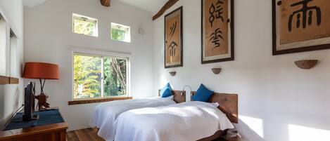 A room with two beds, wooden beams, a window, and Asian calligraphy on the walls.