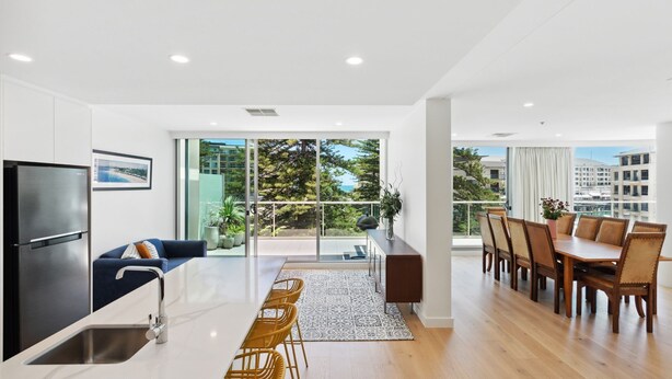 A modern apartment with a kitchen, dining area, and balcony with city views. - Sea the Views (Glenelg)