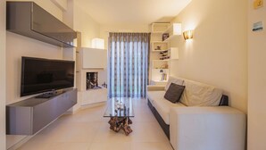 Ein modernes Wohnzimmer mit Flachbildfernseher, Glastisch, weißem Sofa und Kamin.