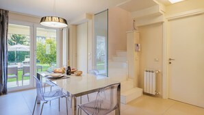 Eine moderne Küche mit großem Esstisch, klaren Stühlen und Blick auf den Garten durch Glastüren.
