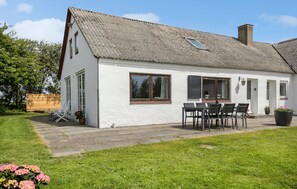 Ein weißes Cottage mit Strohdach, einer Terrasse mit Tisch und Stühlen und einem blühenden Garten.