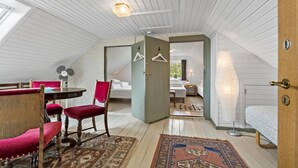Ein gemütliches Schlafzimmer im Dachgeschoss mit Holzbalkendecke, einer Essecke mit Tisch und Stühlen sowie einem großen Fenster für natürliches Licht.