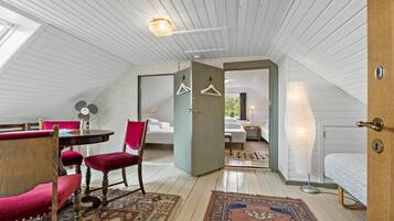 A cozy attic bedroom with a wooden ceiling, a dining area with a table and chairs, and a large window providing natural light.