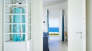 A room with a bed, a wardrobe, and a view of the ocean through a door.