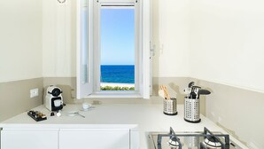 A compact kitchen with a view of the sea, a gas stove, and a coffee maker.
