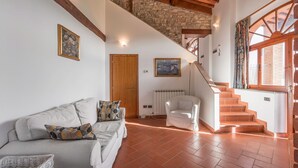 A spacious living room with a sofa, a chair, a staircase, and a view of the outside. - Stunning private villa with private pool, WIFI, A/C, TV, terrace, pets allowed and panoramic view (Greve In Chianti)