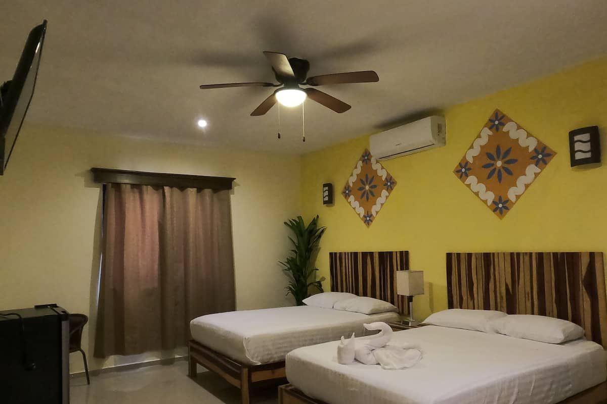 A hotel room with two single beds, a ceiling fan, an air conditioning unit, and a TV.