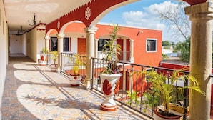 A covered corridor with red arches, potted plants, and a view of a red building.
