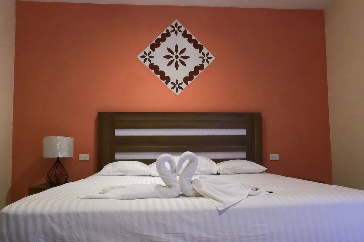 A hotel room with a bed, white linens, a decorative wall piece, and a bedside lamp.