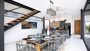Et moderne spiseområde med en trætrappe, et køkken i baggrunden og et spisebord dækket til seks personer.